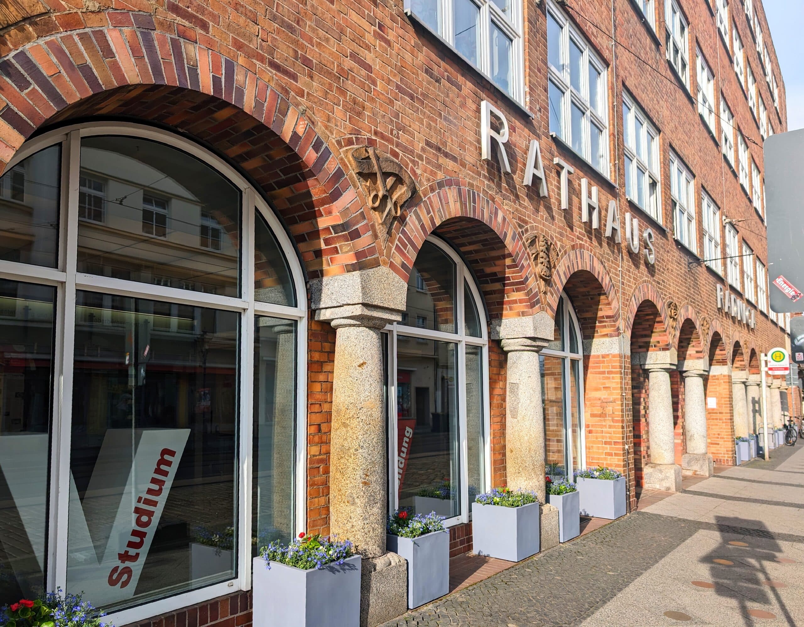 Fassade des Rathauses mit großen Fenstern und Pflanzkästen aus Stein im Vordergrund.